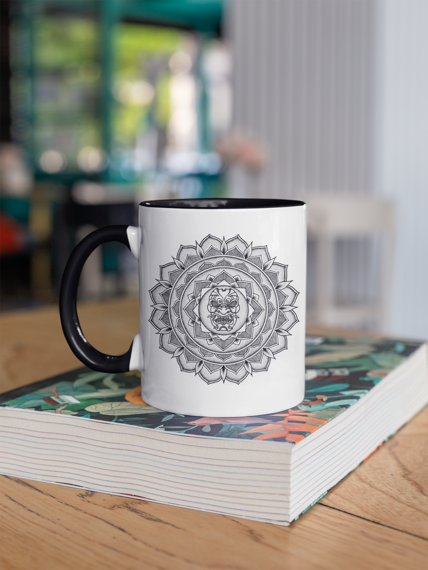 a two toned black and white 11oz coffee mug on a table with a samurai mask mandala design