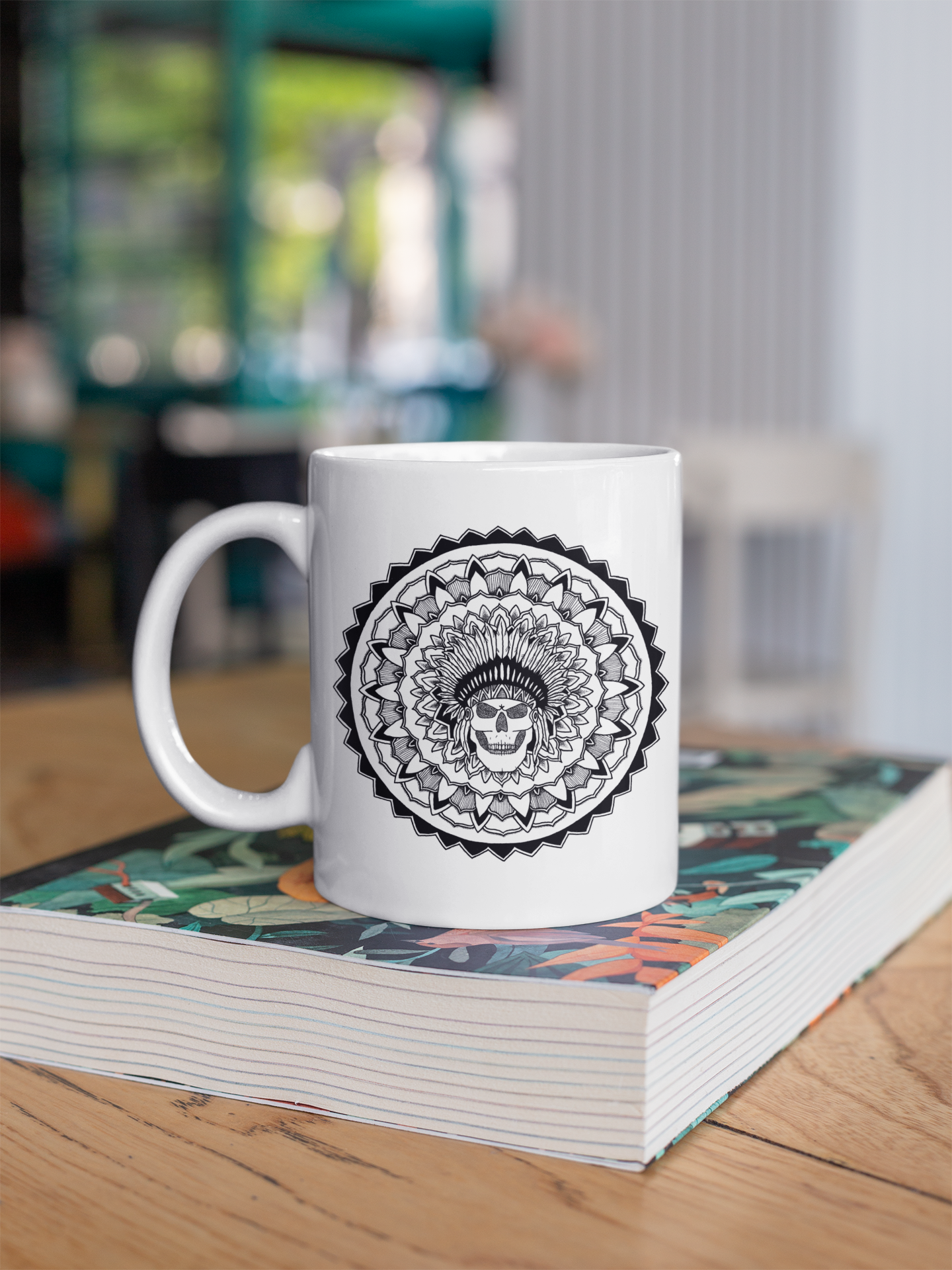 a white 11oz coffee mug with a chieftain skull mandala design resting on a book on a table