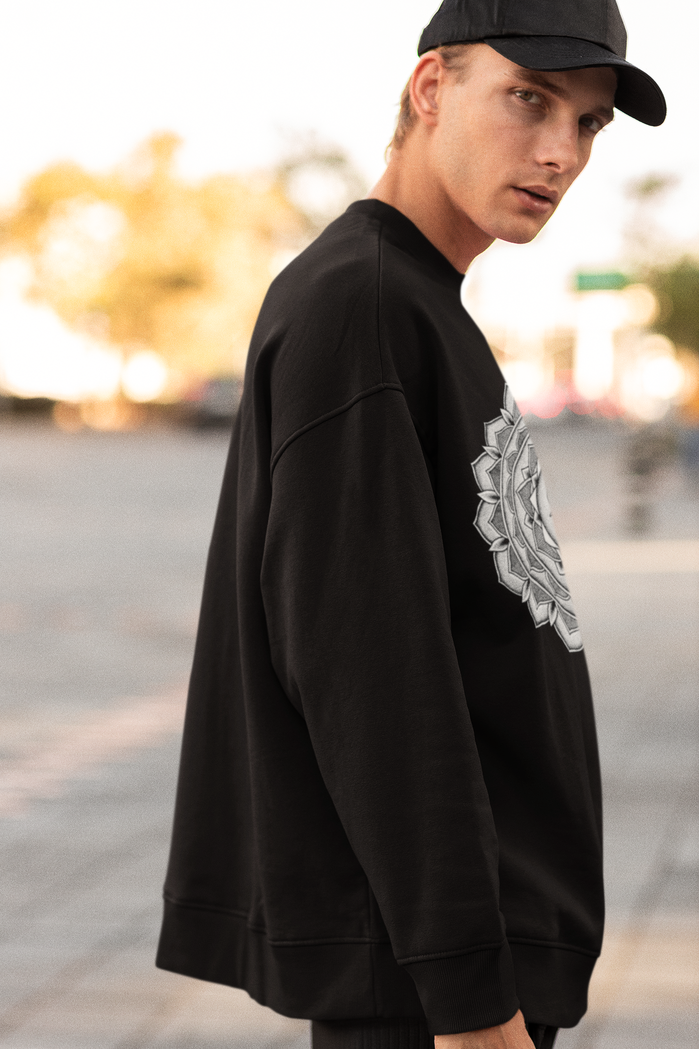 a young man wearing a black baseball cap and a black sweatshirt with a white and black mandala design on the front