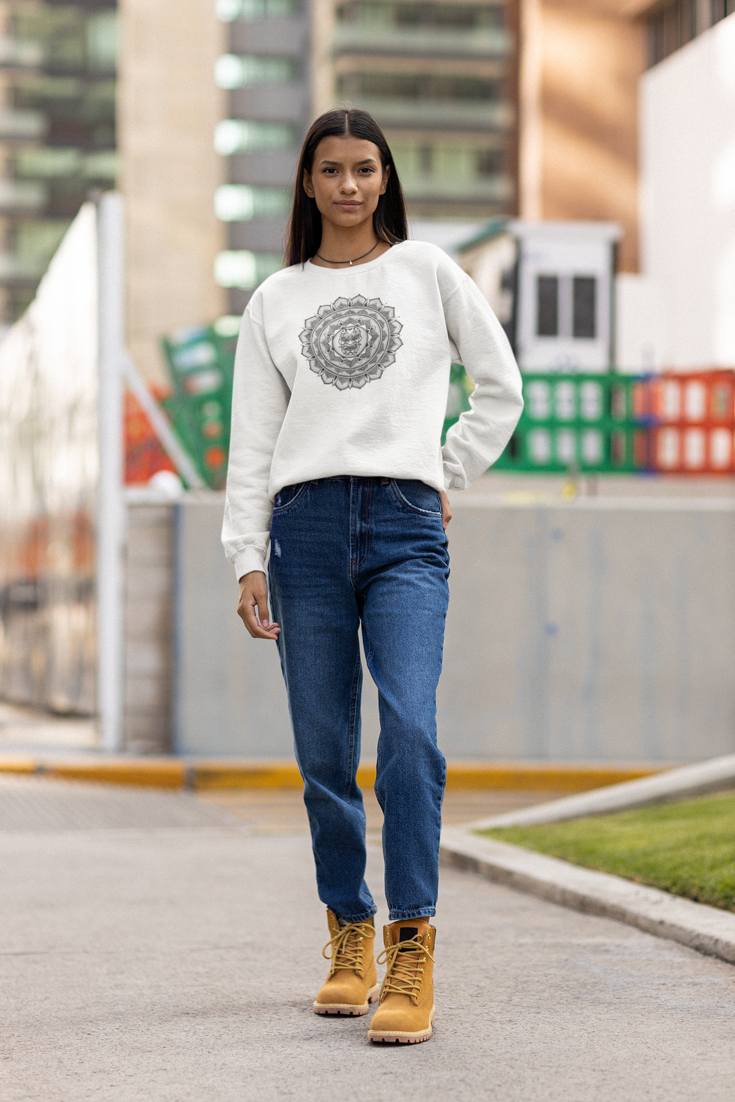 woman in street wearing a white mandalarian brand sweatshirt with a black and white samurai mask design on the front and blue jeans and light suide color boots